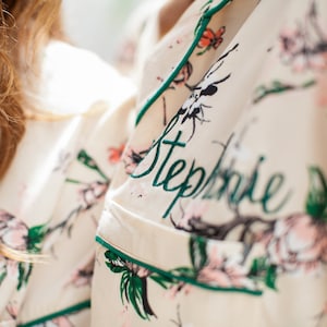 May include: Two white pajamas with floral patterns and green trim. The pajamas are personalized with the names "Elise" and "Stephanie" in green cursive.