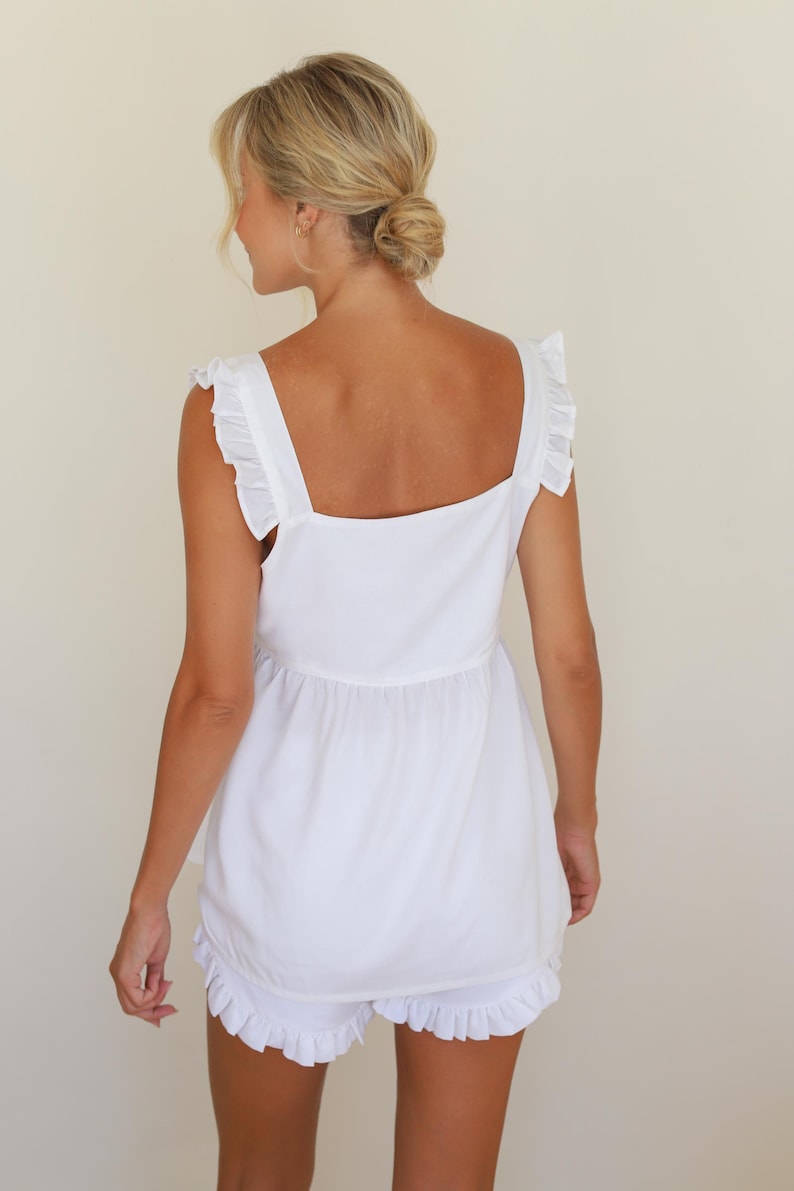 Op de afbeelding: Witte tweedelige set met een top met vierkante halslijn en brede bandjes en bijpassende shorts. De top heeft een geplooid detail in de taille. De shorts hebben een gefranjerde zoom. De outfit is gemaakt van een lichte stof.