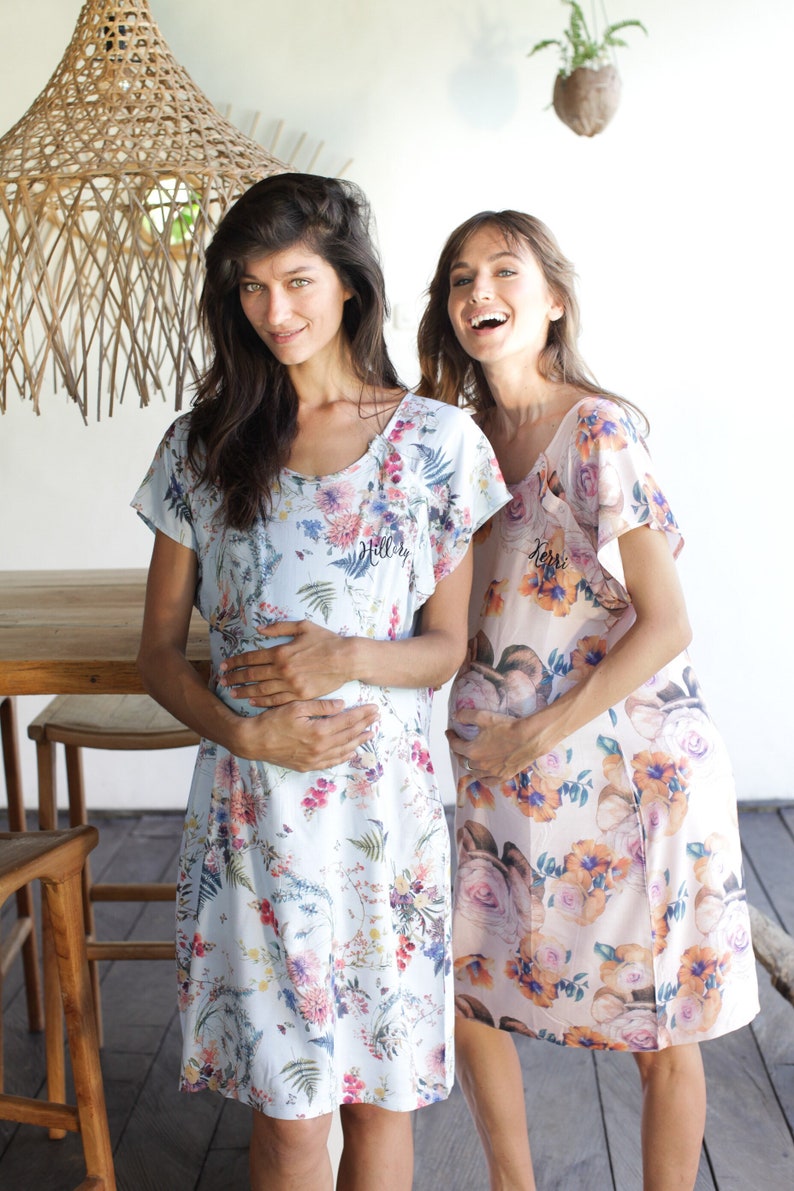 May include: Two people wearing floral print maternity dresses. The dress on the left is light blue with a floral pattern and the text "Hillary" embroidered on the front. The dress on the right is peach with a floral pattern and the text "Kerri" embroidered on the front.