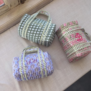 May include: Three small, quilted tote bags in various patterns. One is green and white checkered, another is pink and green floral, and the third is blue with a floral design. Each bag has a handle and embroidered initials.