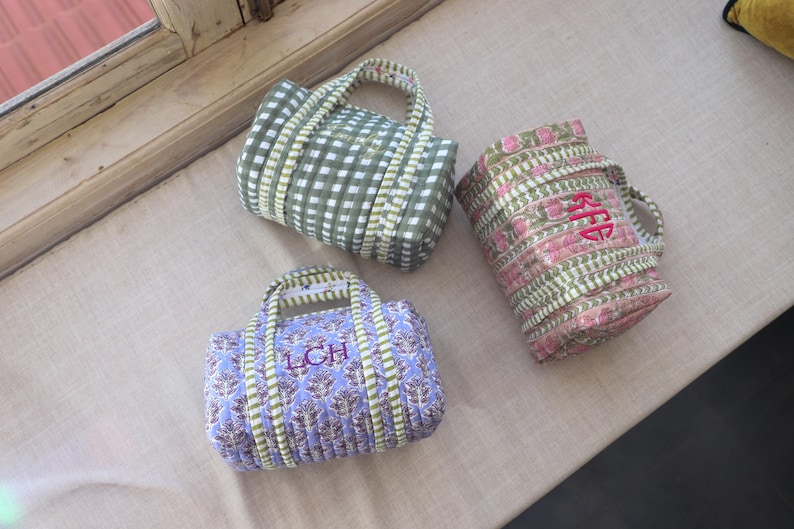 May include: Three small, quilted tote bags in various patterns. One is green and white checkered, another is pink and green floral, and the third is blue with a floral design. Each bag has a handle and embroidered initials.