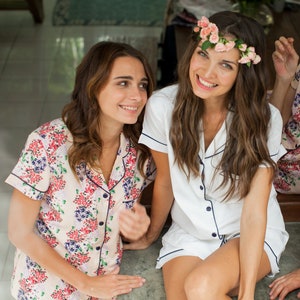 Op de afbeelding: Twee vrouwen in bijpassende bloemen- en witte pyjama's met een bloemenkrans op het hoofd van een van de vrouwen.