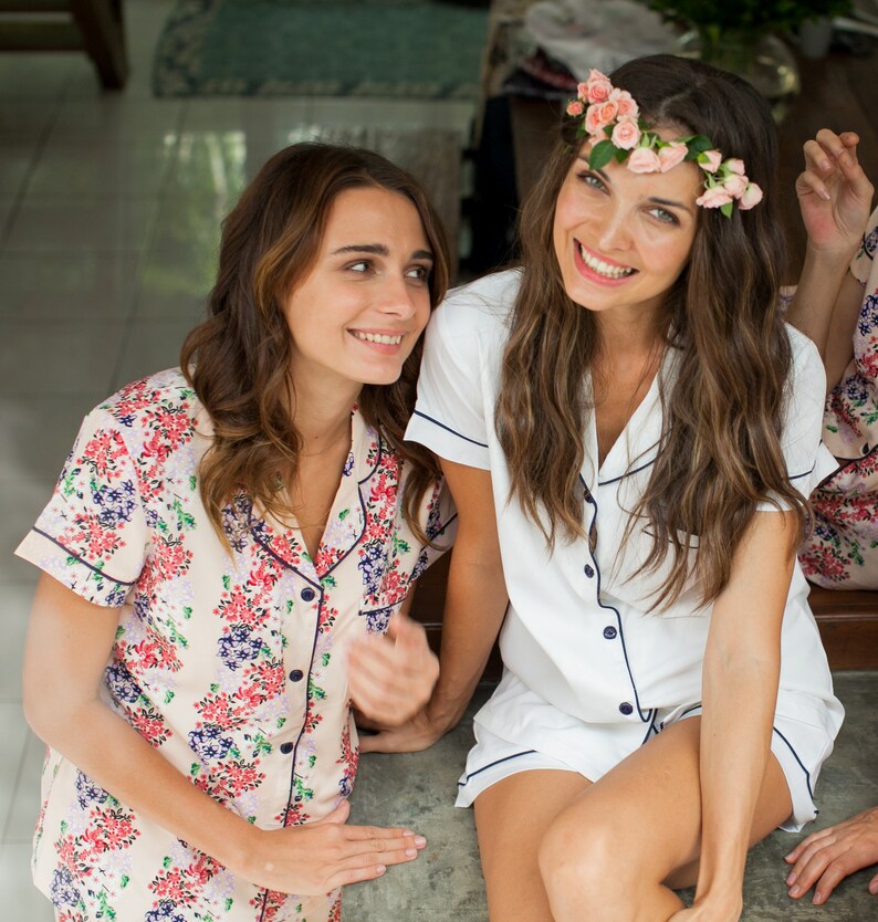 Op de afbeelding: Twee vrouwen in bijpassende bloemen- en witte pyjama's met een bloemenkrans op het hoofd van een van de vrouwen.