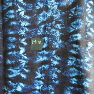 K&ouml;nnte beinhalten: Ein Stoff mit einem dunkelblauen und schwarzen Batikmuster. Der Stoff hat ein florales Design und den Text "M-02" auf einem kleinen Quadrat. Der Stoff wird wahrscheinlich f&uuml;r Kleidung oder Heimdekoration verwendet.