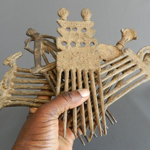 May include: A set of five antique bronze combs with intricate designs. The combs have a variety of shapes and sizes, including a comb with a human figure on the top. The combs are made of a dark brown metal and have a worn, aged appearance.