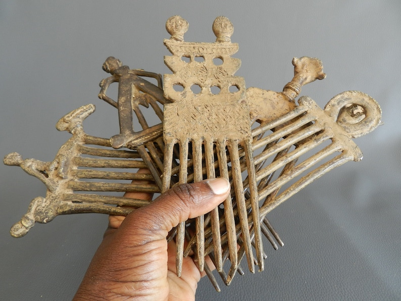 May include: A set of five antique bronze combs with intricate designs. The combs have a variety of shapes and sizes, including a comb with a human figure on the top. The combs are made of a dark brown metal and have a worn, aged appearance.