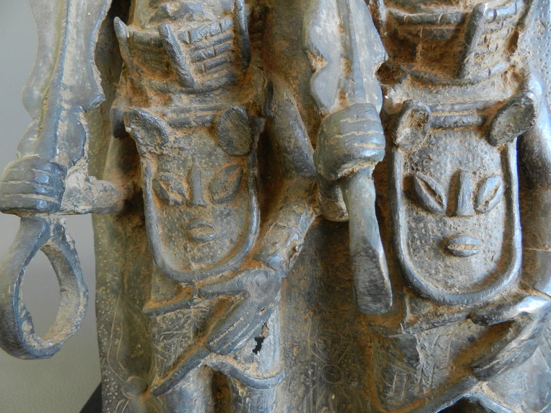 May include: A close-up of a dark gray stone sculpture of two figures. The figures are wearing elaborate headdresses and clothing. The sculpture is highly detailed and has a weathered appearance.