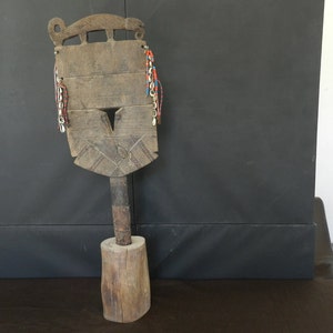 Peut inclure: Objet cérémoniel en bois avec un visage sculpté et une frange de perles. L'objet est monté sur une base en bois.
