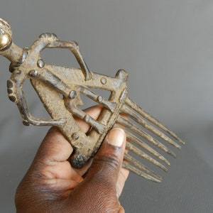 May include: A bronze comb with a human figure design. The comb has seven teeth and is about 6 inches long.