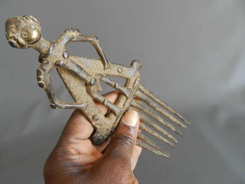 May include: A bronze comb with a human figure design. The comb has seven teeth and is about 6 inches long.