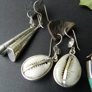 May include: Three pairs of silver earrings with different designs. One pair features a silver cone shape, another pair has a white shell design, and the third pair has a turquoise stone.