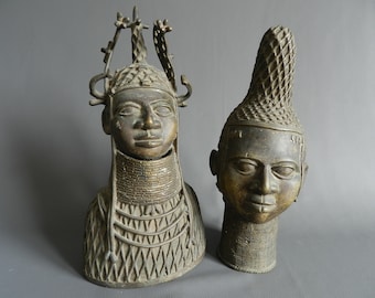 May include: Two bronze sculptures of human heads with intricate details. The sculptures are both wearing elaborate headdresses and necklaces.