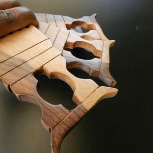 Puede incluir: Un conjunto de tres lanzaderas de tejido de madera apiladas con un patr&oacute;n de veta de madera natural en tonos marr&oacute;n claro y oscuro. Cada lanzadera tiene una secci&oacute;n superior rectangular plana con ranuras horizontales y un dise&ntilde;o de mango recortado.