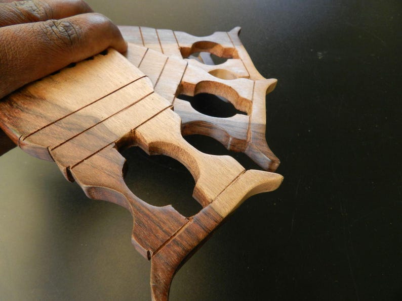 Puede incluir: Un conjunto de tres lanzaderas de tejido de madera apiladas con un patr&oacute;n de veta de madera natural en tonos marr&oacute;n claro y oscuro. Cada lanzadera tiene una secci&oacute;n superior rectangular plana con ranuras horizontales y un dise&ntilde;o de mango recortado.