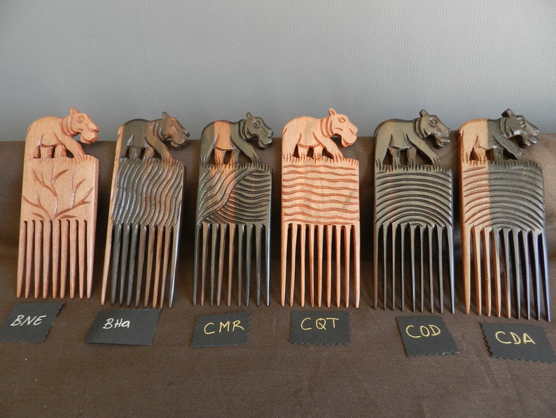 May include: Six wooden combs with carved animal figures on top. The combs are made of dark wood and have a natural finish. The animal figures are all different and include a hippopotamus, a tiger, and a bear. The combs are labeled with the letters BNE, BHA, CMR, CQT, COD, and CDA.