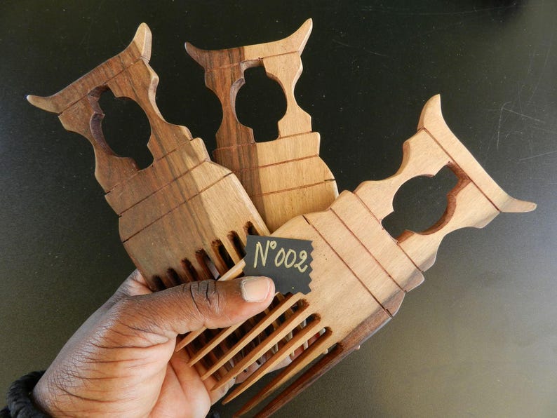 Puede incluir: Tres peines de madera con dientes largos y anchos, y un mango decorativo con un dise&ntilde;o recortado. La madera muestra vetas naturales de color marr&oacute;n. Una peque&ntilde;a etiqueta negra en el centro muestra el texto escrito a mano N&deg;002.