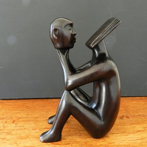 Può includere: Una scultura in legno scuro di una persona seduta con la testa tra le mani. La scultura è astratta e stilizzata.