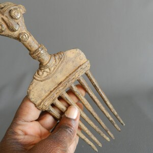May include: A bronze comb with a detailed human-like head handle. The comb has seven teeth and is in a worn condition.