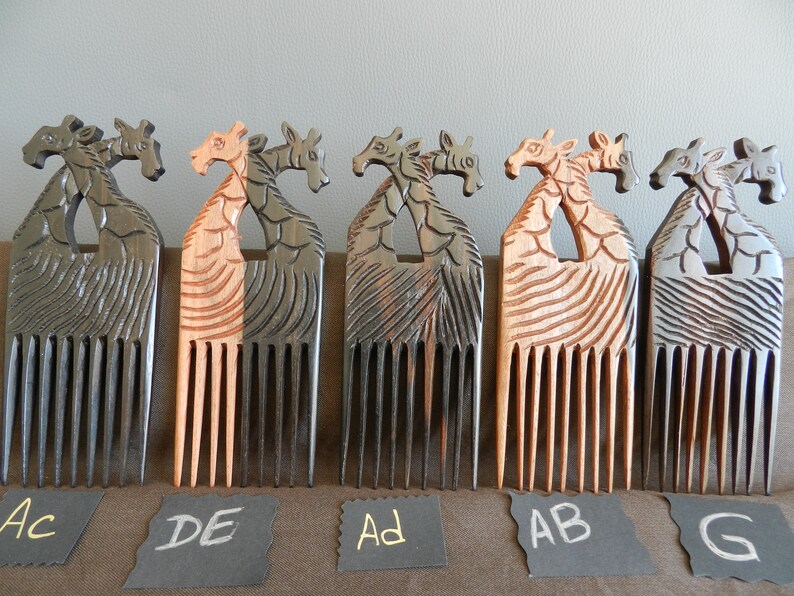 May include: Five wooden combs with giraffe head handles. The combs are in different shades of brown and black. The combs are labeled with letters: AC, DE, AD, AB, and G.