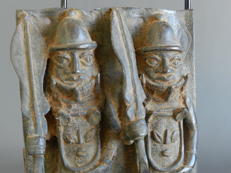 May include: Two bronze sculptures of warriors wearing helmets and holding spears. The sculptures are in a relief style and have a weathered patina.