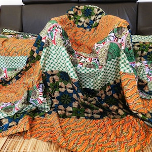 Puede incluir: Una colcha de retazos colorida con una variedad de patrones geométricos y florales en tonos de naranja, verde, azul y blanco. La colcha está hecha de diferentes telas cosidas juntas para crear un diseño único y llamativo.