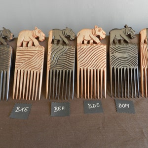 May include: Six wooden combs with a carved hippopotamus design on the top. The combs are in different shades of brown and black. The combs are labeled with the letters BIZ, BXE, BEH, BDE, BOM, and BEE.