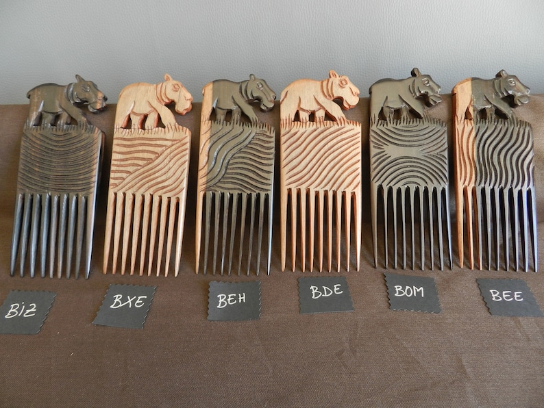May include: Six wooden combs with a carved hippopotamus design on the top. The combs are in different shades of brown and black. The combs are labeled with the letters BIZ, BXE, BEH, BDE, BOM, and BEE.