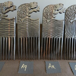 May include: Four wooden combs with carved animal designs. The combs are dark brown and have a natural wood finish. The animal designs are of a lizard or reptile. The combs are labeled with the letters "Aj", "Aq", "Ar", and "Av".