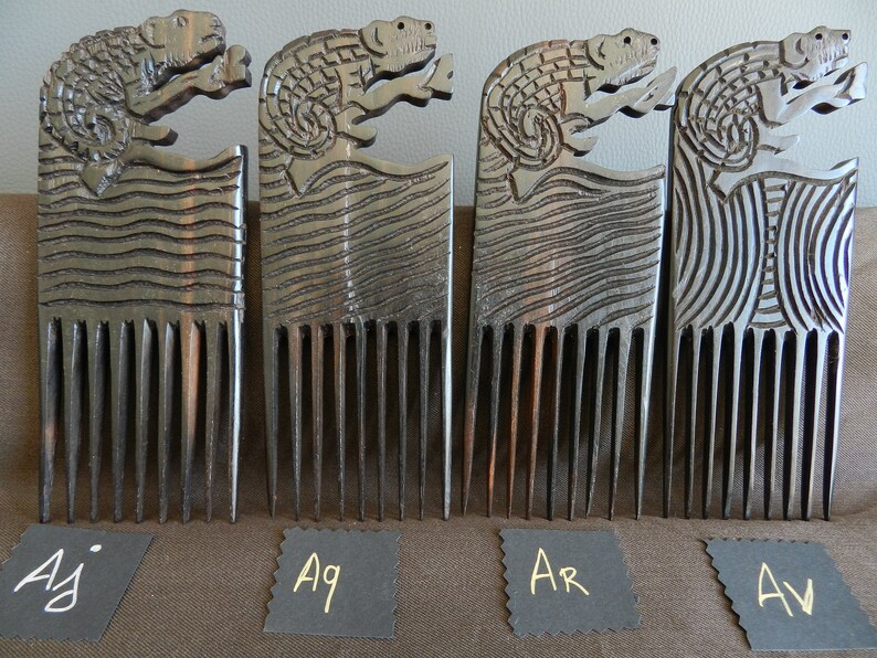 May include: Four wooden combs with carved animal designs. The combs are dark brown and have a natural wood finish. The animal designs are of a lizard or reptile. The combs are labeled with the letters "Aj", "Aq", "Ar", and "Av".