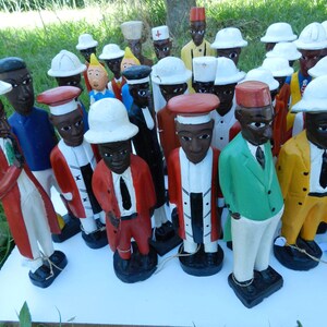 Puede incluir: Una colecci&oacute;n de figuras de madera pintadas a mano que representan a varios personajes con vestimenta profesional diversa, incluyendo sombreros blancos, chaquetas coloridas y corbatas, sobre una superficie blanca. Cada estatua tiene rasgos faciales distintos.