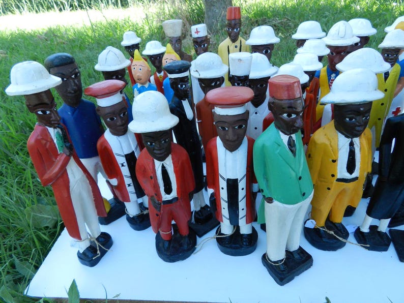Puede incluir: Una colecci&oacute;n de figuras de madera pintadas a mano que representan a varios personajes con vestimenta profesional diversa, incluyendo sombreros blancos, chaquetas coloridas y corbatas, sobre una superficie blanca. Cada estatua tiene rasgos faciales distintos.