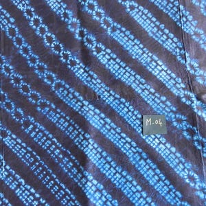 K&ouml;nnte beinhalten: Nahaufnahme eines Textils mit dunkelblauem Hintergrund und diagonalen Streifen in einem helleren Blauton. Die Streifen weisen ein sich wiederholendes Muster aus kleinen Kreisen und Quadraten auf. Ein kleines Etikett mit dem Text "M-04" ist sichtbar.