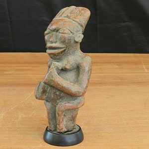 Puede incluir: Una pequeña estatua de madera tallada a mano que representa a una persona con un tocado. La estatua está pintada en tonos marrones y tiene un diseño simple y estilizado.