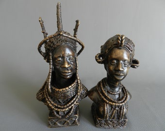Peut inclure: Deux sculptures en bronze de têtes de personnes avec des coiffures et des colliers élaborés. Les sculptures sont de couleur bronze foncé et ont une finition texturée.