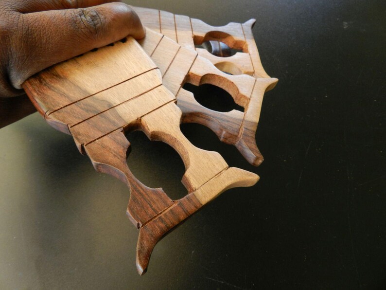 Puede incluir: Un conjunto de tres herramientas de tejido de madera de mano con vetas naturales en tonos marr&oacute;n claro y oscuro. Cada herramienta tiene un cuerpo plano y rectangular con cuatro ranuras horizontales paralelas y un recorte ovalado central.