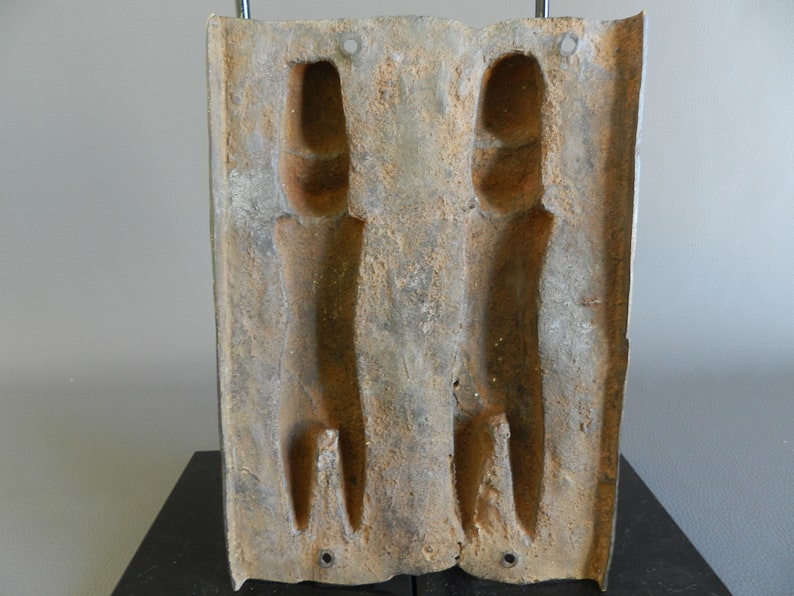 May include: A rectangular, brown, metal mold with two long, narrow, rectangular cavities. The mold is used to create two identical objects.
