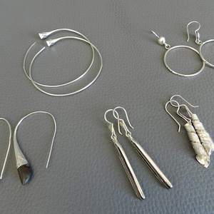 May include: Five pairs of silver earrings. Two pairs are hoop earrings, one pair is a simple drop earring, one pair is a drop earring with a twisted design, and one pair is a drop earring with a black stone.