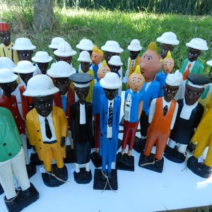Puede incluir: Una colecci&oacute;n de figuras de madera pintadas a mano que representan varios personajes con trajes, sombreros y corbatas coloridos. Cada figura se apoya sobre una base rectangular negra, mostrando atuendos variados con chaquetas amarillas, verdes, azules y naranjas.