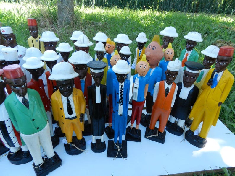 Puede incluir: Una colecci&oacute;n de figuras de madera pintadas a mano que representan varios personajes con trajes, sombreros y corbatas coloridos. Cada figura se apoya sobre una base rectangular negra, mostrando atuendos variados con chaquetas amarillas, verdes, azules y naranjas.