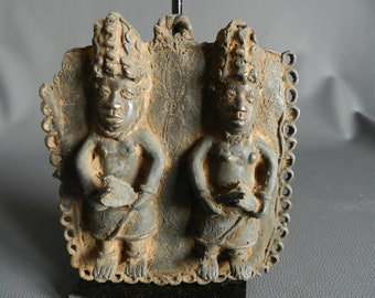 Pode incluir: Uma escultura de bronze de duas figuras com penteados elaborados. As figuras estão de pé lado a lado e estão segurando objetos em suas mãos. A escultura é decorada com uma borda de desenhos intrincados.
