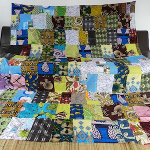 Può includere: Una trapunta colorata a patchwork realizzata con diversi tessuti con motivi e colori diversi. La trapunta è composta da quadrati e rettangoli di tessuto ed è disposta su un tappetino intrecciato.