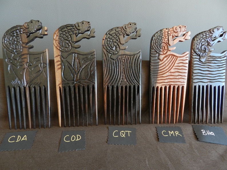May include: Five wooden combs with carved lizard designs. The combs are in different shades of brown, black, and blue. The combs are labeled with the abbreviations CDA, COD, CQT, CMR, and BHa.