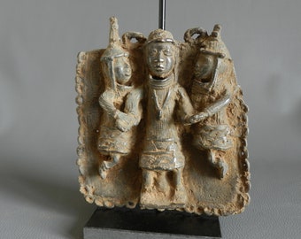 Puede incluir: Una escultura de bronce de tres figuras, dos mujeres y un hombre, de pie juntos. Las figuras visten ropa tradicional y tienen tocados elaborados. La escultura está montada sobre un soporte negro.