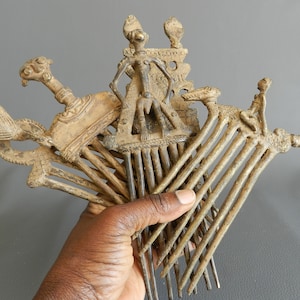 May include: A set of antique bronze combs with intricate designs. The combs feature a variety of figures, including a standing figure with a crown, a seated figure, and a bird. The combs are made of a dark bronze metal and have a worn, aged appearance.