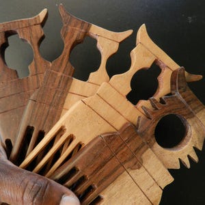 Puede incluir: Una colecci&oacute;n de cuatro peines de madera con mangos tallados que presentan protuberancias en forma de cuerno y recortes circulares. Los peines muestran diversos tonos de veta de madera marr&oacute;n, desde el beige claro al chocolate oscuro, con dientes anchos.