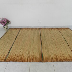 Könnte beinhalten: Ein natürlicher gewebter Teppich in hellbrauner Farbe mit grünen und roten Streifen. Der Teppich ist aus natürlichen Materialien gefertigt und hat einen rustikalen Look.