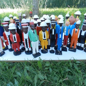 Puede incluir: Una colecci&oacute;n de numerosas figuras de madera pintadas a mano que representan a individuos con diversos atuendos profesionales, incluyendo trajes, sombreros y uniformes en colores vibrantes como rojo, amarillo, azul, verde y negro, sobre una tabla blanca.