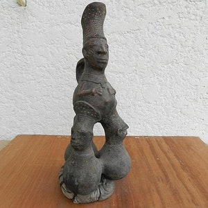 Peut inclure: Une sculpture en céramique d'une personne avec un chapeau haut et pointu. La personne se tient debout sur deux autres figures, toutes de couleur brune et ornées de sculptures détaillées.