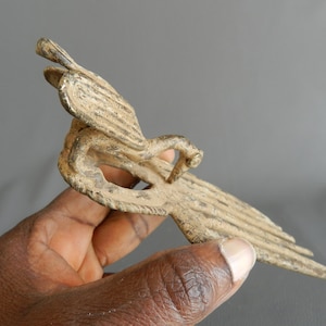 May include: A bronze bird sculpture with intricate details. The bird is depicted in flight with its wings spread wide. The sculpture is made of a dark bronze metal and has a weathered finish.