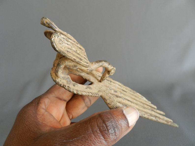 May include: A bronze bird sculpture with intricate details. The bird is depicted in flight with its wings spread wide. The sculpture is made of a dark bronze metal and has a weathered finish.
